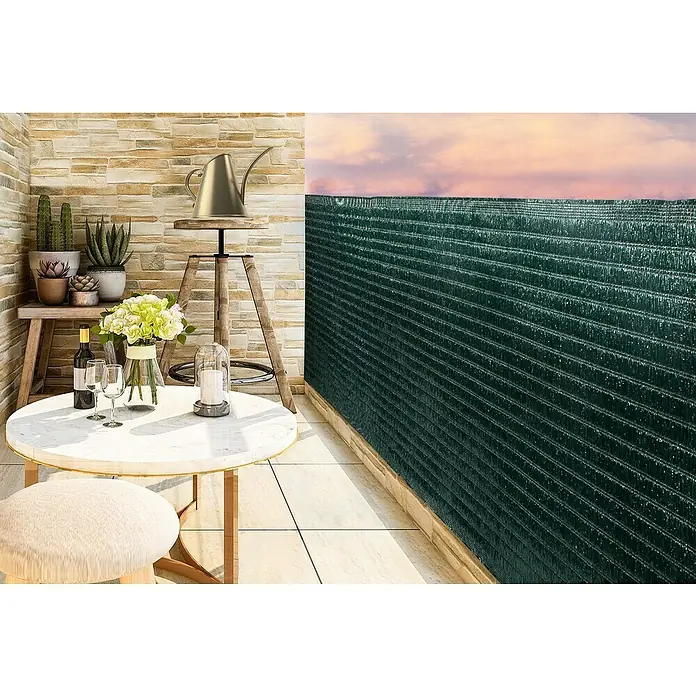 Gardol Balkonsichtschutz Raffia - Grün, 300 x 90 cm - Ein stilvoller Balkon mit Tisch, Stuhl, Pflanzen und Sichtschutz, der Privatsphäre bietet und die Aussicht auf einen farbenfrohen Himmel ermöglicht.
