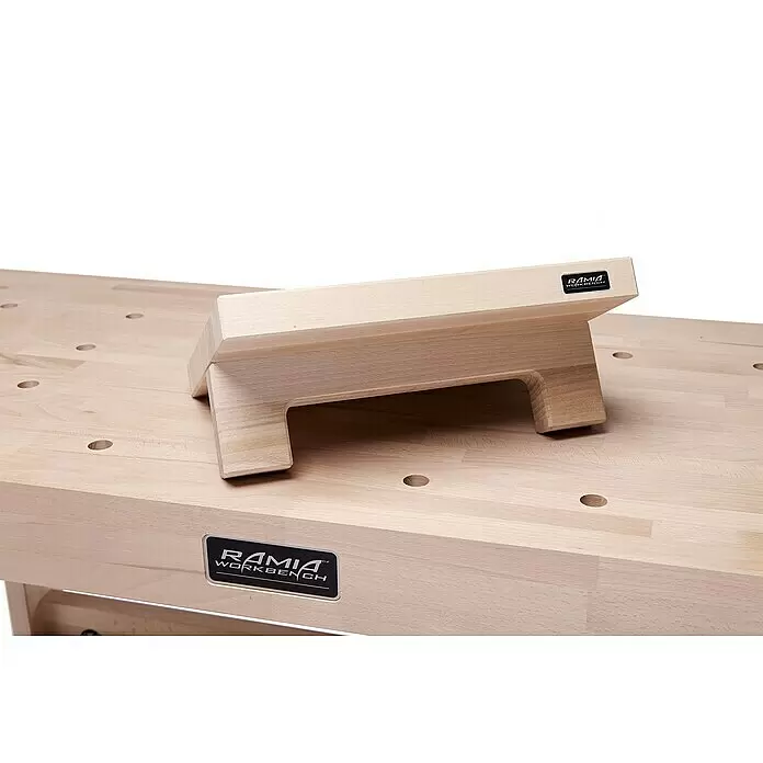 Ramia Werkbank-Zubehör Universalauflage - Passend für: Ramia Werkbänke - Heller Holz-Werkbankanschlag mit Logo auf einer hellen Holz-Werkbank mit runden Löchern.