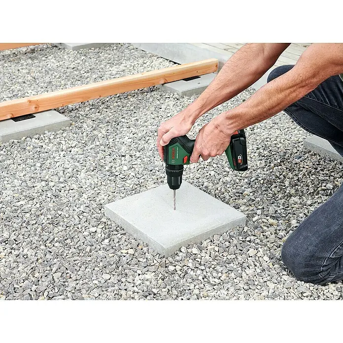 Bosch Power for All 18V Akku-Schlagbohrschrauber UniversalImpact 18V-60 - 18 V, 2 Akkus, 2 Ah - 4 Ah, 60 Nm - Nahaufnahme einer Person, die mit einem Bosch Akku-Bohrschrauber ein Loch in eine quadratische Betonplatte bohrt.