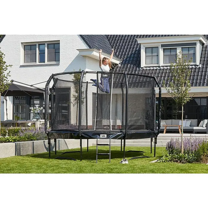 Salta Trampolin First Class - Durchmesser: 366 cm, Schwarz - Mädchen springt auf einem rechteckigen Salta-Trampolin im Garten, umgeben von Grün. Ein Spaß für Kinder.
