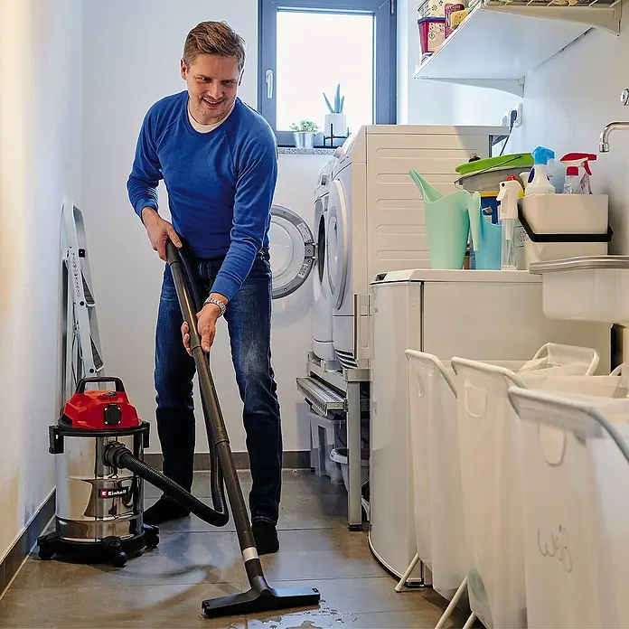Einhell Elektro-Nass- & Trockensauger TC-VC 1820 SA - 1.250 W, 20 l - Ein Mann saugt mit einem Einhell Nass-Trockensauger Wasser in einem Waschraum auf. Der Sauger ist rot und silber.