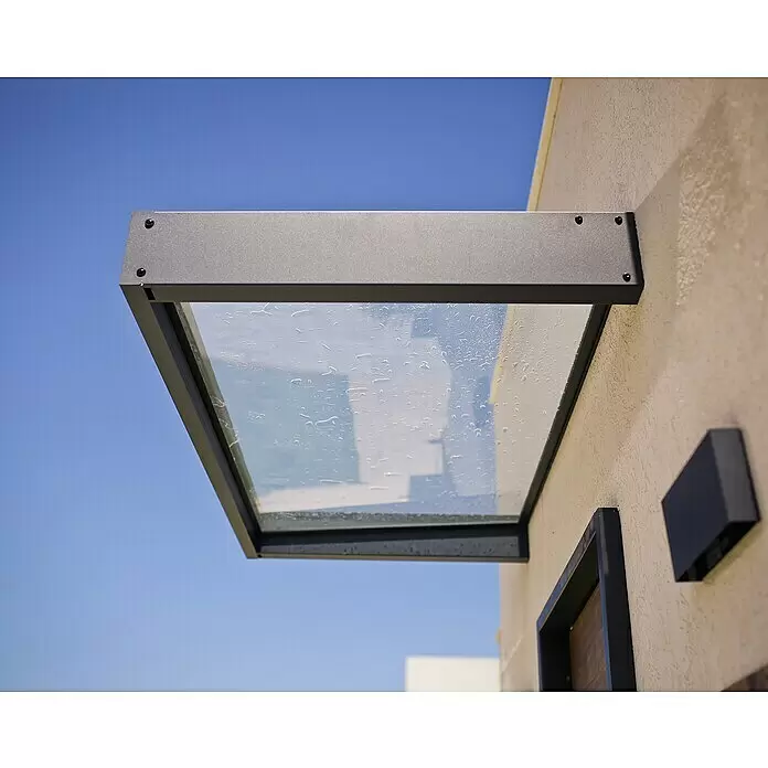 Palram – Canopia Pultvordach Sophia - 160 x 95 x 17 cm, Anthrazitgrau, Farbe Dach: Klar - Dunkelgraues Vordach aus Metall und Glas mit Wassertropfen, an einer Gebäudewand montiert.