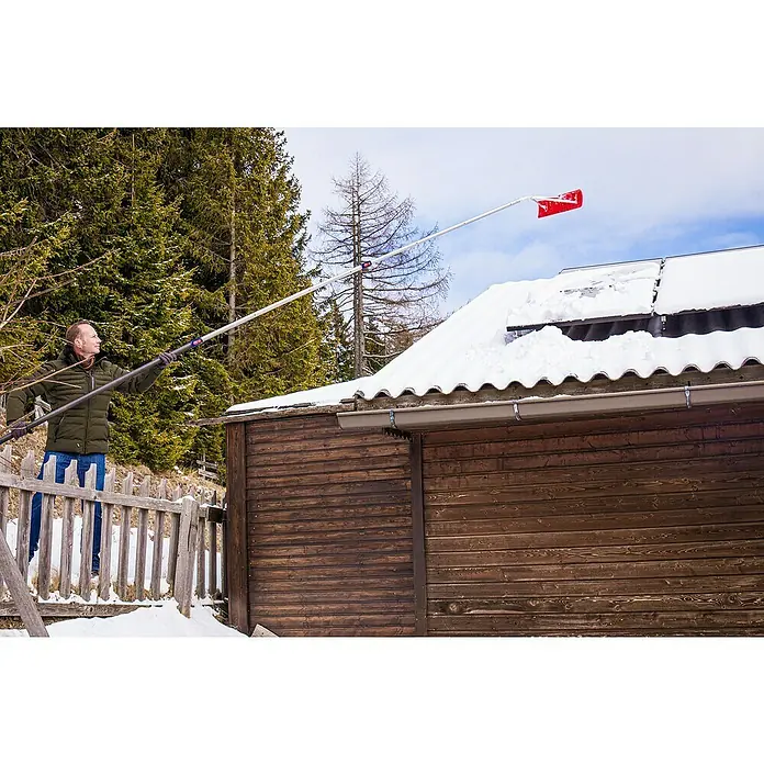 Freund Victoria Schneeschieber Dachräumer - Breite: 60 cm, Teleskopstiel - Mann entfernt Schnee vom Dach eines Holzschuppens mit einem Schneerechen, der an einer langen Stange befestigt ist.
