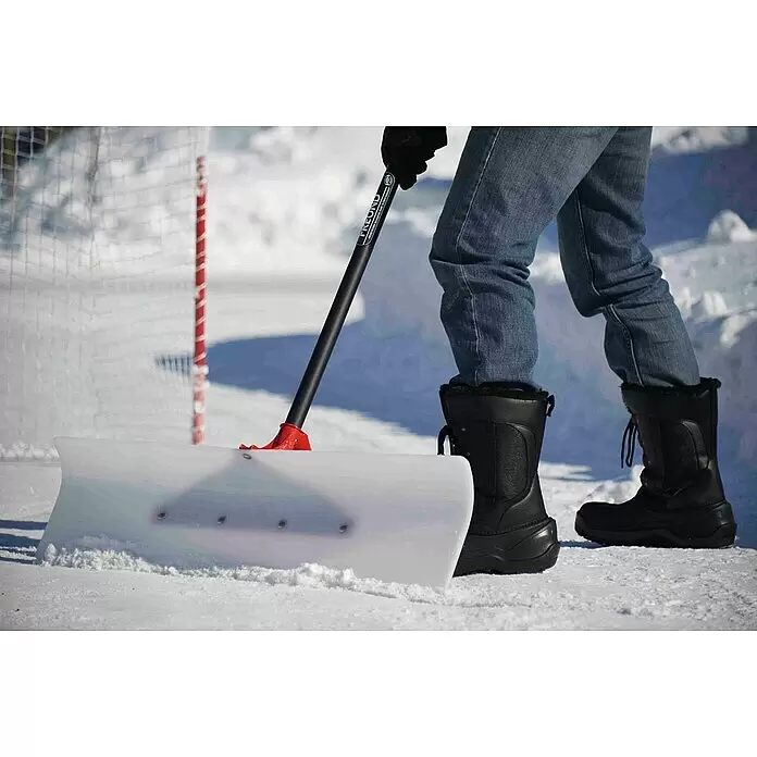 Freund Victoria Schneeschieber Snow pusher - Breite: 61 cm, Langstiel - Eine Person räumt Schnee von einer Eisbahn mit einem Schneeschieber mit schwarzem Griff, rotem Verbinder und weißer Klinge.