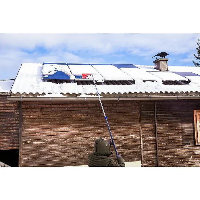 Freund Victoria Schneeschieber Dachräumer - Breite: 60 cm, Teleskopstiel - Eine Person entfernt Schnee von Solarmodulen auf einem Dach mit einem Schneerechen, um die Energieerzeugung zu optimieren.