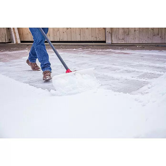 Freund Victoria Schneeschieber Snow pusher - Breite: 61 cm, Langstiel - Person räumt Schnee mit einer weißen und roten Schneeschaufel auf einem gepflasterten Bereich.