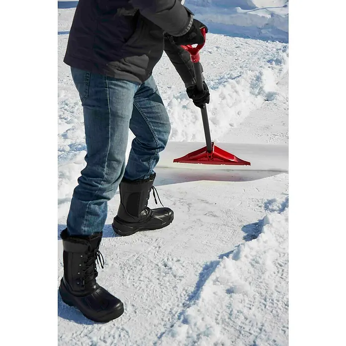 Freund Victoria Schneeschieber Snow pusher - Breite: 61 cm, Langstiel - Ein Mann schiebt mit einem roten Schneeschieber Schnee auf einer schneebedeckten Fläche. Er trägt Winterstiefel, Jeans und eine dunkle Jacke.