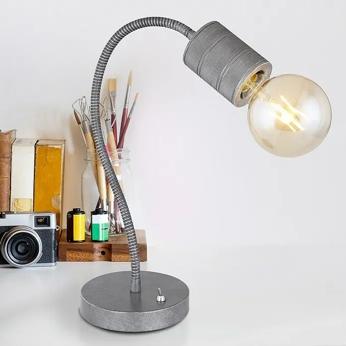 Globo Freddy Tischleuchte rund - 60 W, Silber, E27 - Nahaufnahme einer silberfarbenen Schreibtischlampe mit einem runden Lampenschirm und einer Edison-Glühbirne auf einem Schreibtisch mit Büchern.
