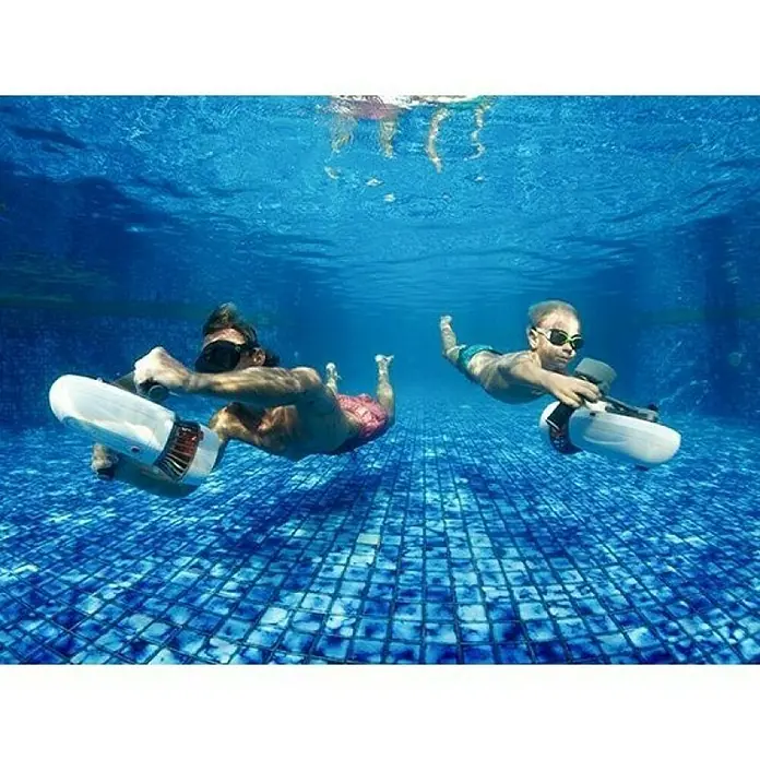 Sublue Tauchscooter Tini - L x B x H: 355 x 135 x 135 mm - Zwei Personen tauchen mit Unterwasser-Scootern im Pool. Die Geräte sind weiß und ermöglichen eine mühelose Fortbewegung unter Wasser.