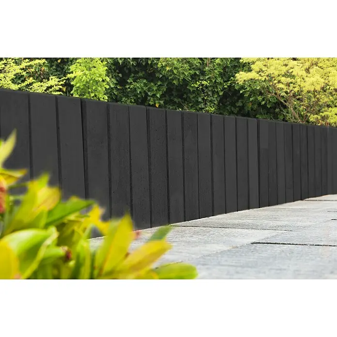 Diephaus Palisade / Mauerstein Laredo Meso - 80 x 12,5 x 12,5 cm, Basalt, Beton - Schwarzer Betonzaun mit vertikalen Rillenstruktur, umgeben von Grünpflanzen. Die Zaunelemente sind schlicht und modern gestaltet.