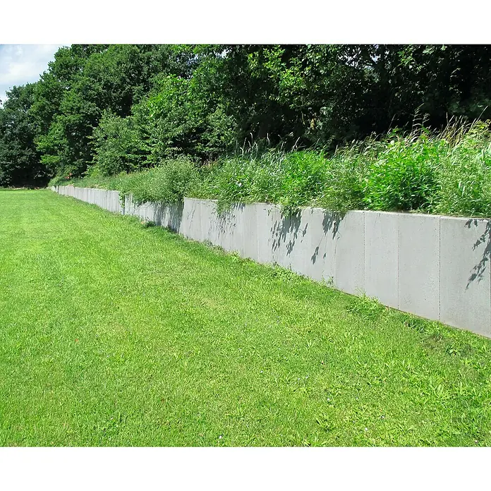 Diephaus L-Stein - 80 cm, 40 cm, Stärke: 7 cm, Grau - Eine lange, graue Betonmauer, die einen Rasen von einem bewachsenen Bereich trennt. Die Mauer ist schlicht und funktional.
