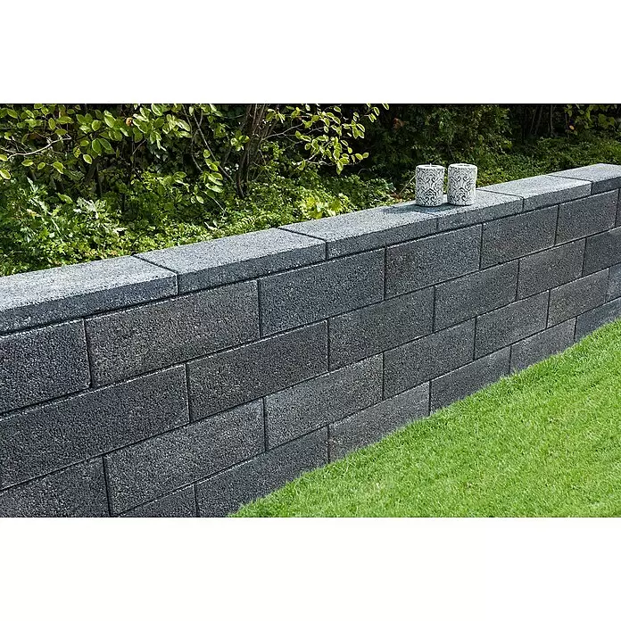 Diephaus Mauerstein Logan - 45 x 22,5 x 16,5 cm, Quarzit, Beton - Dunkelgraue, texturierte Gartenmauer mit zwei dekorativen weißen Kerzenhaltern.