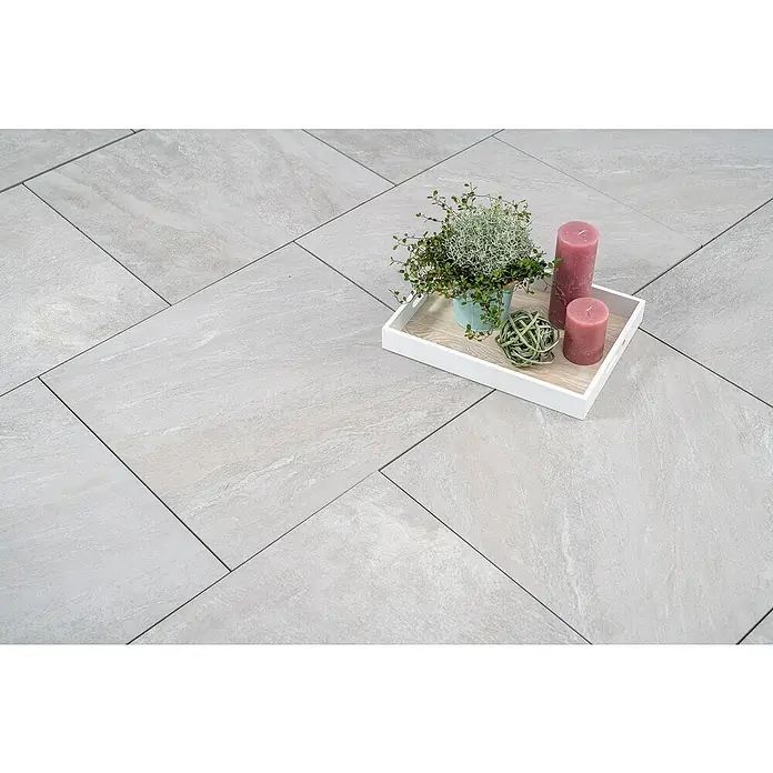 Diephaus Terrassenfliese Columbia - 60 x 60 x 4 cm, Quarz, Beton - Elegante graue Bodenfliesen mit einem Dekorationsarrangement aus Kerzen, Topfpflanze und Zierkugel auf einem weißen Tablett.