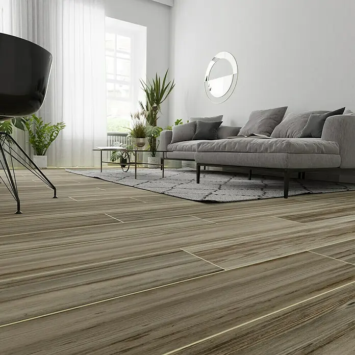 Feinsteinzeugfliese Betulla - 20 x 120 cm, Braun, Matt - Ein stilvolles Wohnzimmer mit Holzbodenfliesen, einem grauen Sofa und Pflanzen, die eine gemütliche Atmosphäre schaffen. Die Holzbodenfliesen sind sehr attraktiv.