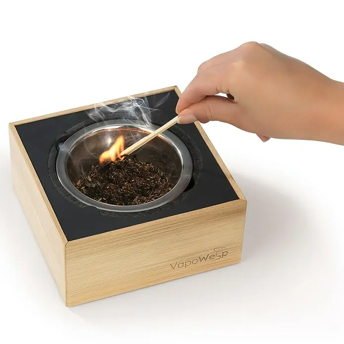 VapoWesp Räucherpulver - Orange & Rosemary, 100 g - Ein quadratischer VapoWesp-Räucherbehälter aus Holz mit einer Hand, die mit einem Streichholz Räucherstäbchen anzündet.