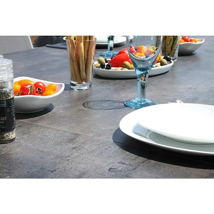 Acamp Gartenmöbel-Set Urban/Extensio - 5 -tlg., Aluminium, HPL, Textil, Klappbar, Anthrazit - Nahaufnahme von Speisen auf einem Esstisch, darunter Tomaten, Grissini, Oliven und einem blauen Glas, die eine einladende Tischszene ergeben.