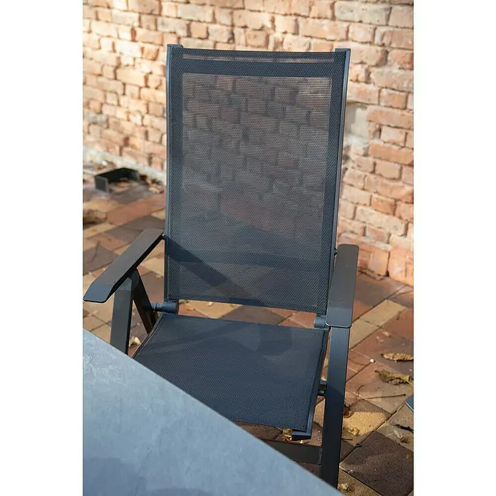 Acamp Klappstuhl Urban - Aluminium, Textil, Rückenlehne verstellbar, Anthrazit, B x T x H: 60 x 66 x 112 cm - Nahaufnahme eines modernen Gartenstuhls aus schwarzem Metall mit Netzgewebe vor einer Ziegelmauer.