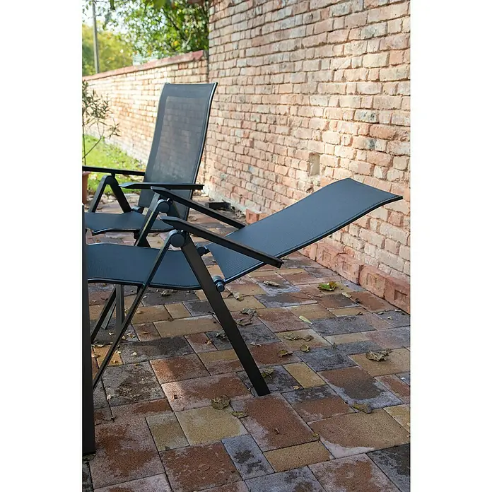 Acamp Klappstuhl Urban - Aluminium, Textil, Rückenlehne verstellbar, Anthrazit, B x T x H: 60 x 66 x 112 cm - Aufnahme von zwei Liegestühlen aus schwarzem Metall auf einer Terrasse mit bunten Ziegeln. Der Fokus liegt auf den robusten und wetterfesten Möbeln.