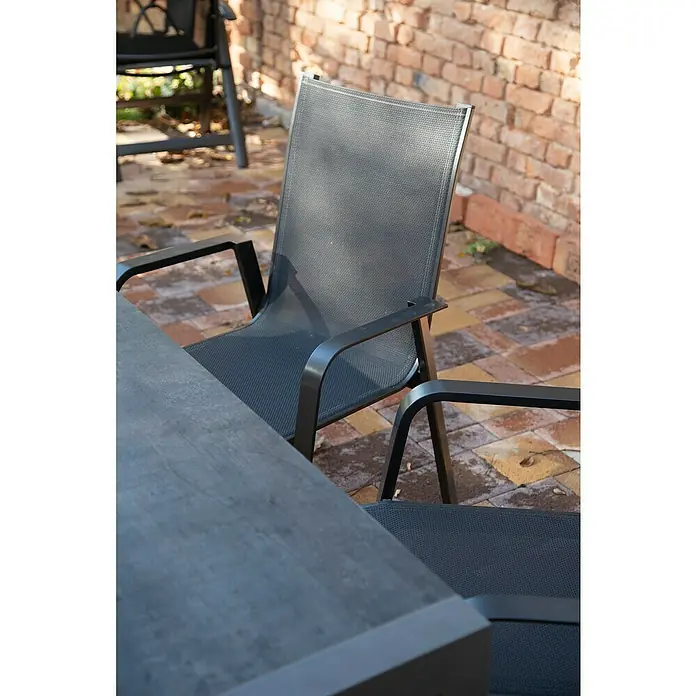 Acamp Gartenmöbel-Set Urban - 5 -tlg., Aluminium, HPL, Acatex, Grau - Nahaufnahme eines grauen Gartenstuhls mit Armlehnen und Netzstoffbespannung vor einer Ziegelmauer und einem Tisch.