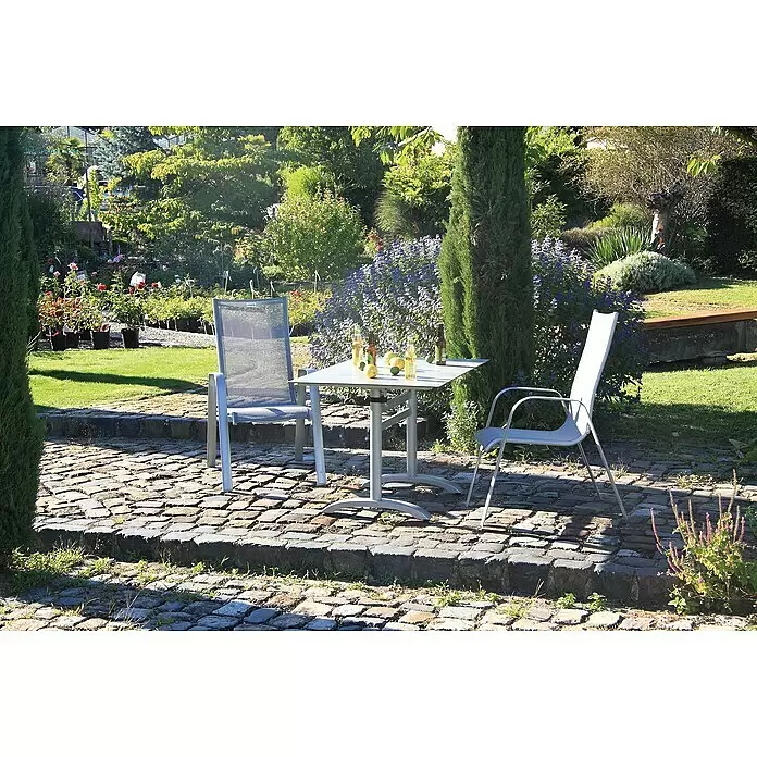 Acamp Gartentisch Acaplan - L x B x H: 120 x 80 x 72 cm, Aluminium, HPL, Rechteckig, Silber - Heller grauer Terrassentisch und zwei Stühle auf einer Kopfsteinpflasterterrasse in einem sonnigen Garten, ein Stuhl mit gestreifter Rückenlehne.
