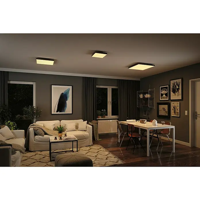 Paulmann LED-Panel Velora Rainbow - 16 W, L x B x H: 29,5 x 29,5 x 6,4 cm, Schwarz, RGBW - Das Bild zeigt ein Wohnzimmer mit einer modernen Deckenleuchte, die ein warmes Licht spendet. Die Leuchte ist quadratisch und fügt sich nahtlos in das Raumdesign ein.