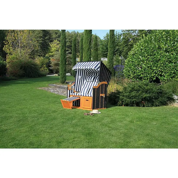 Acamp Strandkorb Sylt - L x B x H: 110 x 81 x 160 cm, Holz, Polyrattan, Blau/Weiß/Grau - Ein Strandkorb mit blau-weißen Streifen steht auf einer grünen Wiese, umgeben von Bäumen und Büschen. Eine idyllische Szene für Entspannung.