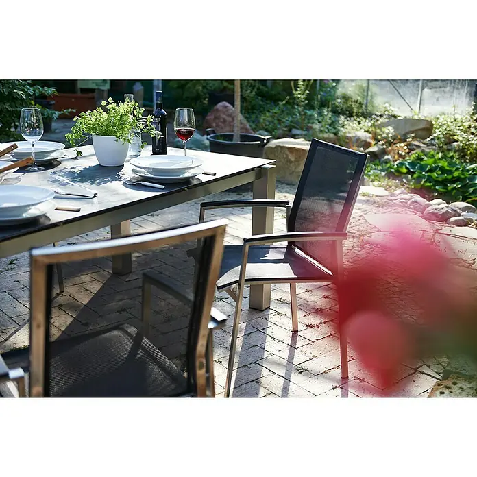 Acamp Gartenmöbel-Set Auris - 5 -tlg., Edelstahl, Polywood, Keramik, Stapelbar, Silber/Schwarz - Ein Gartentisch mit Geschirr, einer Pflanze, einer Flasche Wein und Gläsern, umgeben von Gartenstühlen auf einer Terrasse.
