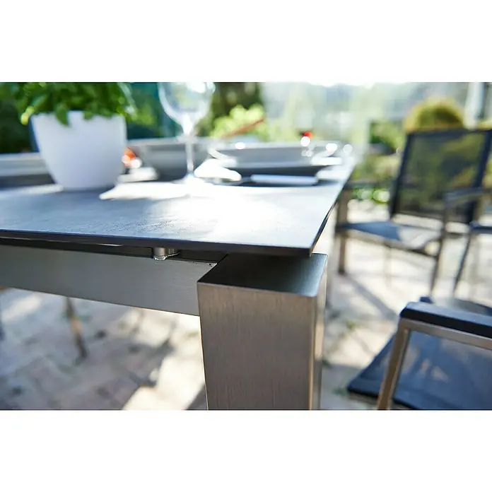 Acamp Gartenmöbel-Set Auris - 5 -tlg., Edelstahl, Polywood, Keramik, Stapelbar, Silber/Schwarz - Nahaufnahme eines Esstisches mit Tischplatte und Metallbeinen, umgeben von Stühlen und Pflanzen im Freien.