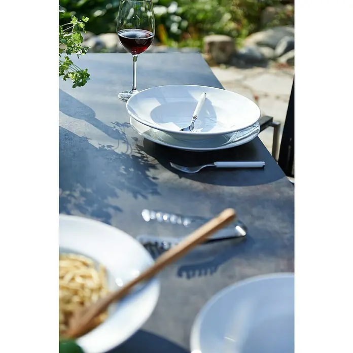 Acamp Gartenmöbel-Set Auris - 5 -tlg., Edelstahl, Polywood, Keramik, Stapelbar, Silber/Schwarz - Ein Esstisch mit Geschirr, Besteck und einem Glas Rotwein, bereit für eine Mahlzeit im Freien.