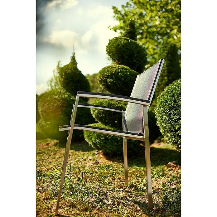 Acamp Gartenmöbel-Set Auris - 5 -tlg., Edelstahl, Polywood, Keramik, Stapelbar, Silber/Schwarz - Eine Nahaufnahme eines modernen Gartenstuhls mit silbernem Rahmen und schwarzer Sitzfläche, der auf einem Rasen vor üppigem Grün steht.