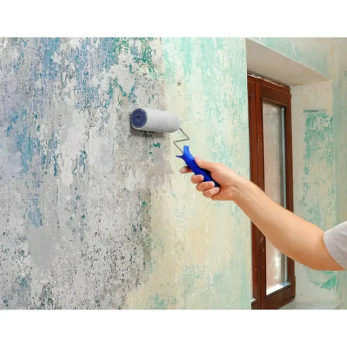 Knauf Rotband Grundierung - 5 kg - Ein Mann streicht eine Wand mit einer Farbwalze. Die Hälfte der Wand ist bereits in einer helleren Farbe gestrichen.