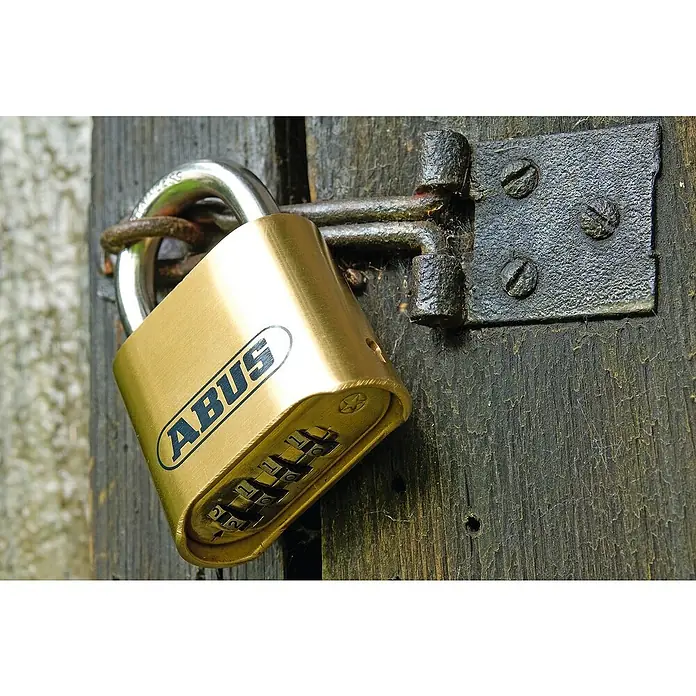 Abus Vorhängezahlenschloss 180IB/50 HB63 - B x L: 52 x 24 mm, Messing, Anzahl Zahlenrollen: 4 Stk., Messing - Nahaufnahme eines ABUS-Vorhängeschlosses mit Zahlencode, das an einem alten, verriegelten Holztor befestigt ist.