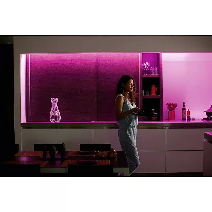 Philips Hue LED-Band Plus Basis - 2 m, RGBW - Eine moderne Küche, beleuchtet mit lebendiger violetter LED-Beleuchtung, die die Atmosphäre verstärkt, während eine Frau Geschirr trägt.