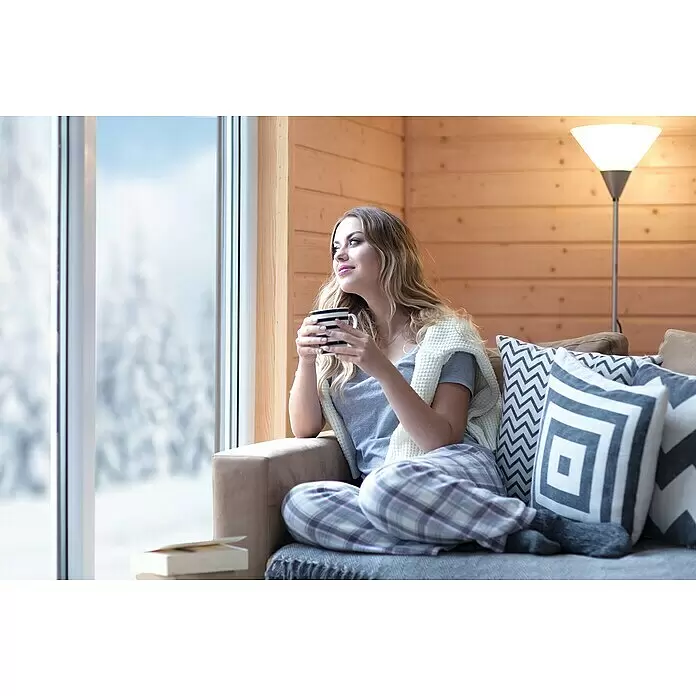 Kombiprofil - 2.000 x 116 x 19 mm, Douglasie, Unbehandelt - Frau in kariertem Schlafanzug und Strickdecke entspannt auf braunem Sofa mit gestreifter Tasse, blickt aus Fenster auf verschneite Landschaft.