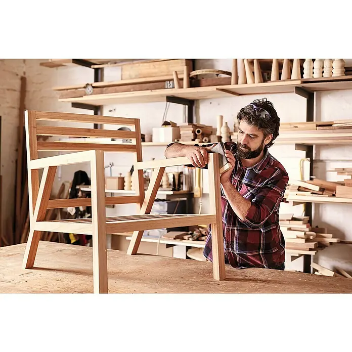 Rahmenholz - 300 x 3,4 x 3,4 cm, Fichte - Ein Tischler bearbeitet einen Holzstuhl in seiner Werkstatt. Der handgefertigte Stuhl steht im Fokus.