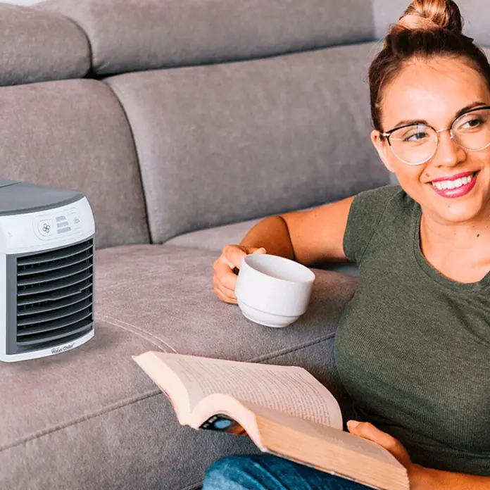 Aire acondicionado portátil Eco Water Chiller - Blanco - Una mujer se relaja en el sofá con el enfriador de aire Arctic Chill, un libro y una taza.