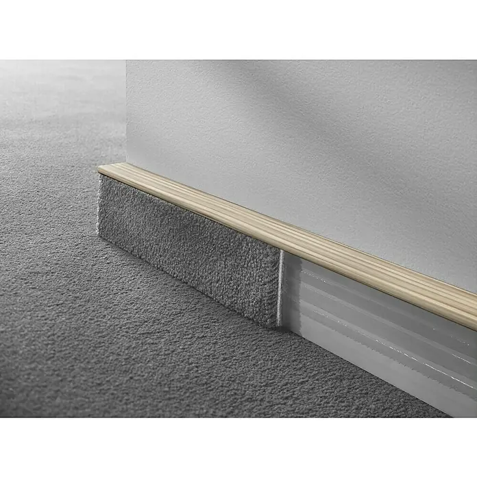 LOGOCLIC Sockelleiste TSL - 250 cm x 16 mm x 55 mm, Esche Weiß - Nahaufnahme von Teppichsockelleisten mit Holzdetails. Die Textur des Teppichs und die saubere Wand werden hervorgehoben.