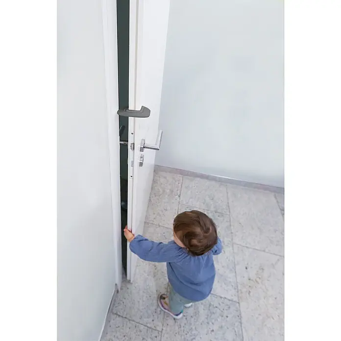 Abus Türstopper Mina - Grau, 2 Stk. - Ein Kind öffnet eine weiße Tür mit zwei Griffen in einem hellen Raum.