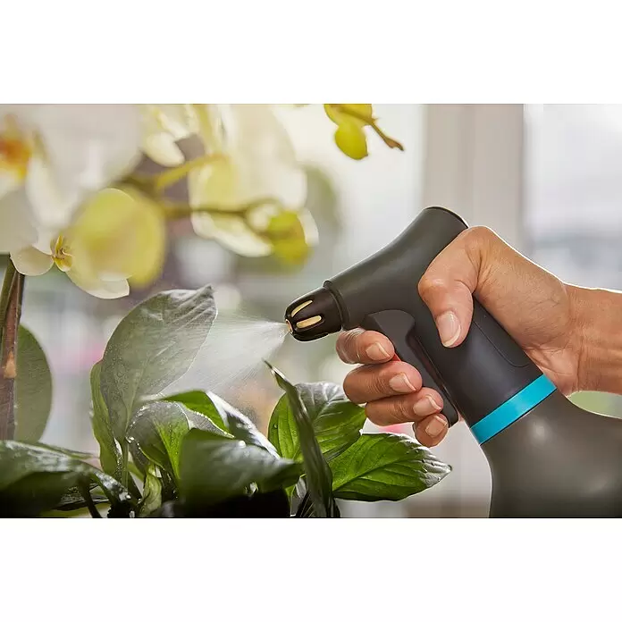 Gardena Handsprüher - Schwarz, 0,75 l - Eine Hand hält eine dunkelgraue Sprühflasche mit blauem Band, die Wasser auf grüne Blätter sprüht. Die Sprühdüse hat gelbe Details.