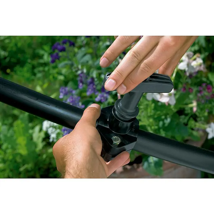 Gardena Sprinklersystem Montagewerkzeug - Passend für: Anbohrschelle 3/4" - Nahaufnahme des Drip-Systems, das mit einer schwarzen Bewässerungsleitung verbunden ist, sowie eines Drehventils zur Wasserflusssteuerung.