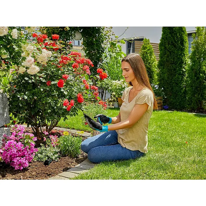 Gardena Gartenhandschuhe Pflanz- und Bodenarbeit - 10, XL, Schwarzblau - Eine Frau im Garten arbeitet mit Gartenhandschuhen an Blumen. Sie trägt Jeans und ein T-Shirt und kniet auf dem Rasen.