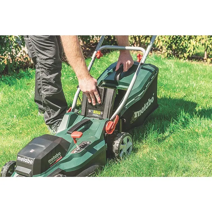 Metabo CAS 18V Akku-Rasenmäher RM 36-18 LTX BL 36 - 18 V, Ohne Akku, 5,2 Ah, Schnittbreite: 36 cm - Ein Mann wechselt den Akku eines Metabo Rasenmähers im Garten. Der Rasenmäher ist grün und hat einen Fangkorb.