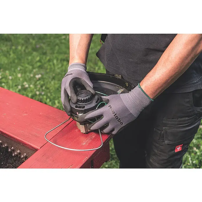 Metabo CAS 18V Akku-Rasentrimmer RTD 18 LTX BL 30 - 18 V, 2 Ah, Ohne Akku, Schnittbreite Faden: 30 cm - Mann wechselt Fadenkopf an einer Motorsense. Im Fokus steht der Fadenkopf mit neuem Faden, der auf einem roten Untergrund liegt.