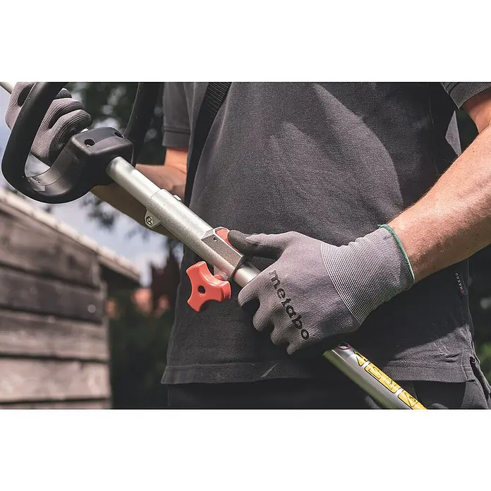 Metabo CAS 18V Akku-Rasentrimmer RTD 18 LTX BL 30 - 18 V, 2 Ah, Ohne Akku, Schnittbreite Faden: 30 cm - Nahaufnahme einer Person mit Metabo-Gartenwerkzeug, die Handschuhe trägt und die Bedienelemente bedient.