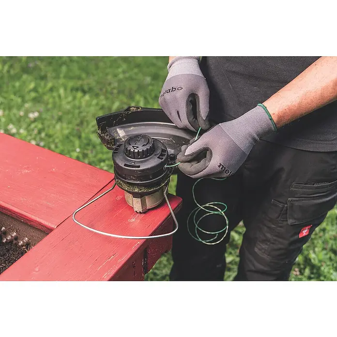 Metabo CAS 18V Akku-Rasentrimmer RTD 18 LTX BL 30 - 18 V, 2 Ah, Ohne Akku, Schnittbreite Faden: 30 cm - Eine Person wechselt die Schnur an einem Metabo Rasentrimmer vor einem grünen Hintergrund.