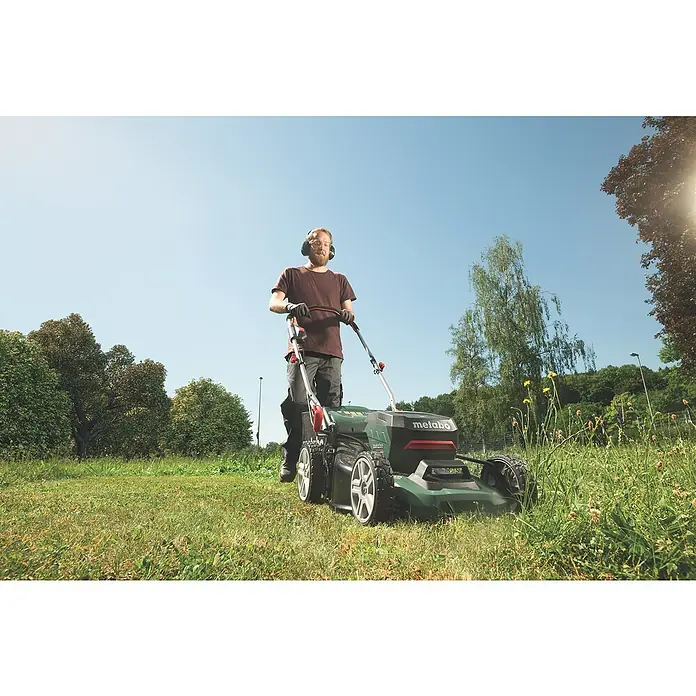 Metabo CAS 18V Akku-Rasenmäher RM 36-18 LTX BL 46 - 18 V, Ohne Akku, 5,2 Ah, Schnittbreite: 46 cm - Ein Mann mäht mit einem Metabo Rasenmäher den Rasen im Garten, ausgestattet mit Gehörschutz und Handschuhen, unter strahlend blauem Himmel.