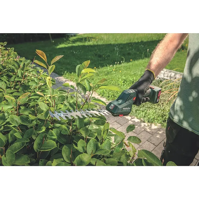 Metabo Akku-Gras- & Strauchschere PowerMaxx SGS 12 Q - 12 V, Li-Ionen, Ohne Akku, Schwertbreite: 13 cm - Nahaufnahme einer Metabo Akku-Grasschere, die an einer Hecke verwendet wird, Fokus auf Präzision und Benutzerfreundlichkeit des Werkzeugs.