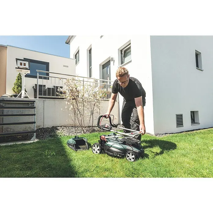 Metabo CAS 18V Akku-Rasenmäher RM 36-18 LTX BL 36 - 18 V, Ohne Akku, 5,2 Ah, Schnittbreite: 36 cm - Ein Mann bereitet einen Metabo Rasenmäher für die Gartenarbeit vor, mit einem modernen Haus im Hintergrund.