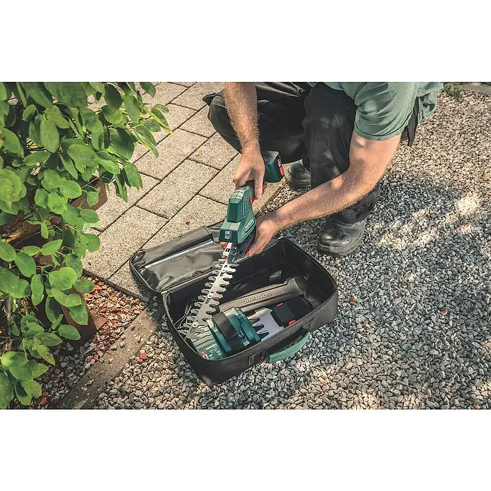 Metabo Akku-Gras- & Strauchschere PowerMaxx SGS 12 Q - 12 V, Li-Ionen, Ohne Akku, Schwertbreite: 13 cm - Ein Mann packt eine Metabo Akku-Strauchschere mit Zubehör in einer schwarzen Tasche auf einem Kiesweg aus.