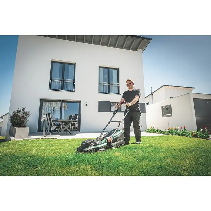 Metabo CAS 18V Akku-Rasenmäher RM 36-18 LTX BL 36 - 18 V, Ohne Akku, 5,2 Ah, Schnittbreite: 36 cm - Ein Mann mäht den Rasen mit einem Metabo Rasenmäher vor einem modernen Haus. Der Rasenmäher ist grün und schwarz.